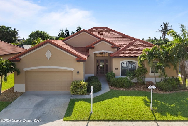 mediterranean / spanish-style home featuring a garage, a tiled roof, a front lawn, and stucco siding