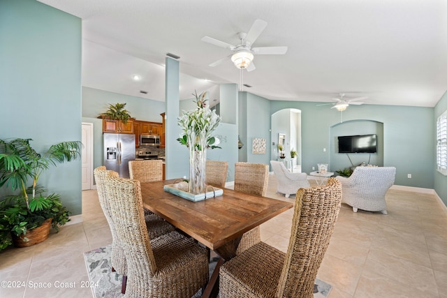 dining room featuring arched walkways, baseboards, ceiling fan, vaulted ceiling, and light tile patterned flooring