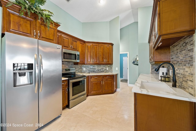 kitchen with light stone counters, stainless steel appliances, a sink, brown cabinets, and tasteful backsplash