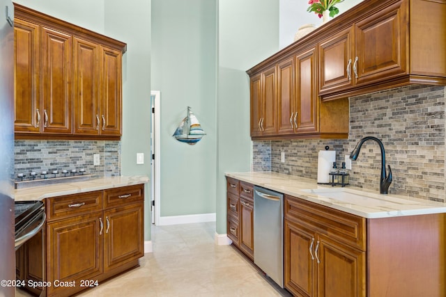 kitchen featuring stainless steel appliances, brown cabinets, a sink, and light stone countertops