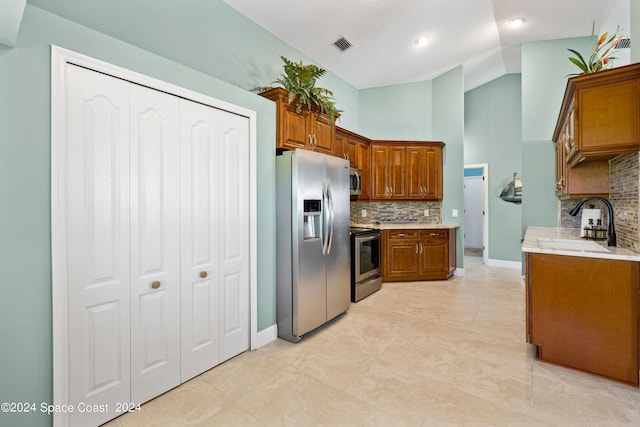 kitchen with stainless steel appliances, light countertops, brown cabinetry, vaulted ceiling, and a sink