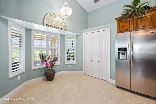 kitchen featuring vaulted ceiling, brown cabinetry, stainless steel refrigerator with ice dispenser, and baseboards