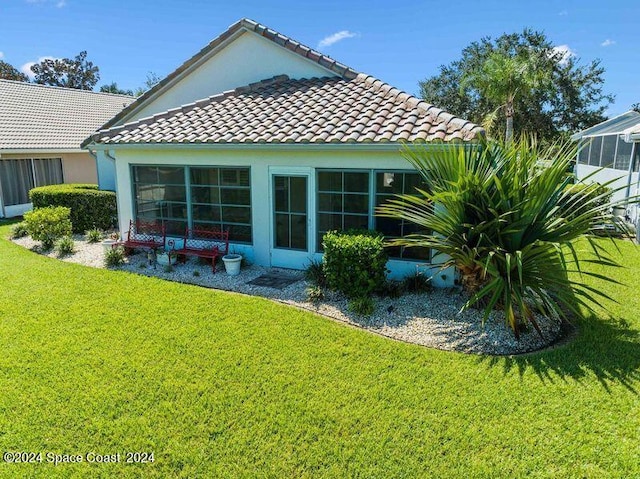 rear view of property featuring a lawn, a tile roof, and stucco siding