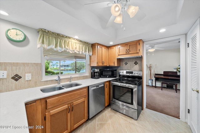 kitchen featuring stainless steel appliances, decorative backsplash, sink, ceiling fan, and light carpet