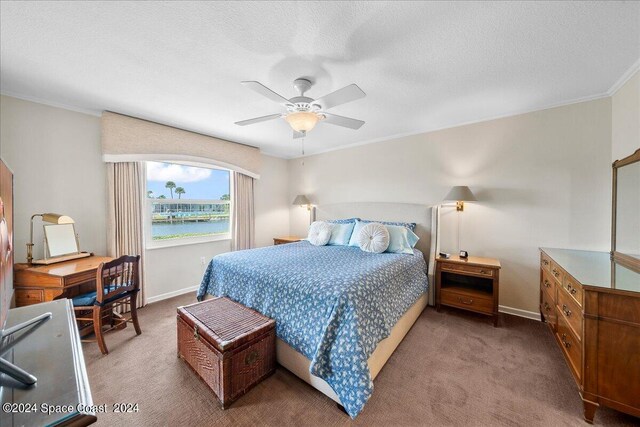 bedroom with ceiling fan, a textured ceiling, carpet floors, crown molding, and a water view