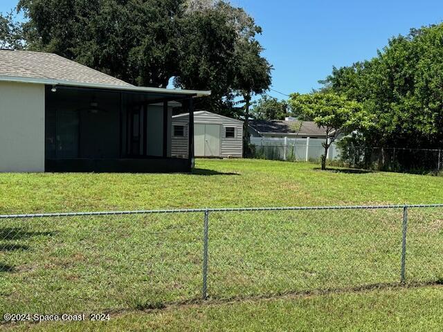 view of yard with a storage shed, an outdoor structure, a fenced backyard, and a sunroom