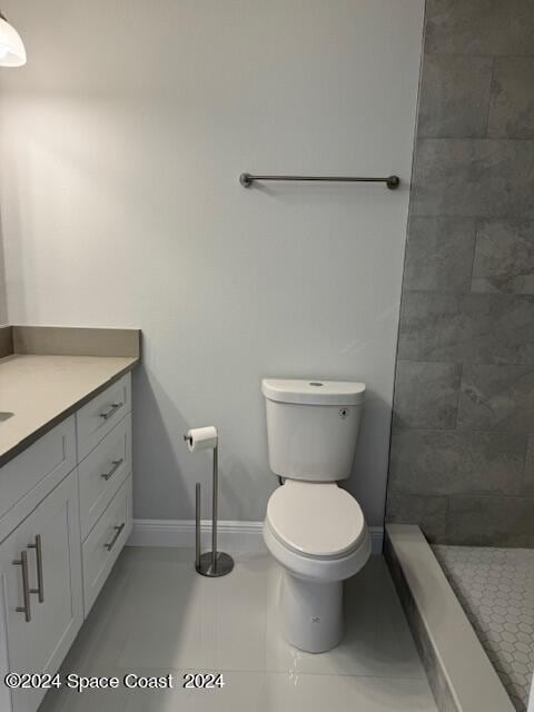 bathroom featuring baseboards, a tile shower, vanity, and toilet