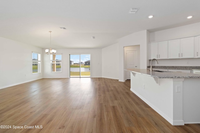 kitchen featuring white cabinets, sink, light stone countertops, wood-type flooring, and a chandelier