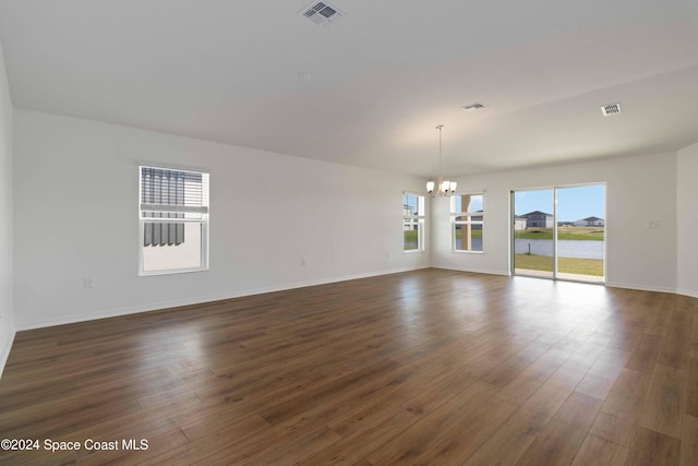 empty room with a notable chandelier and dark hardwood / wood-style floors