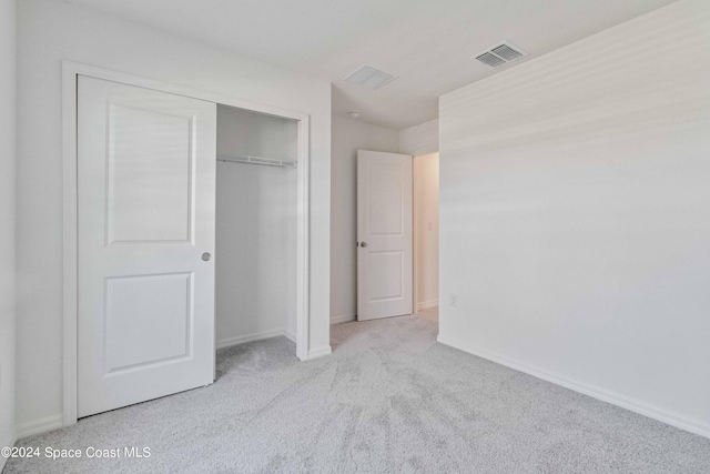 unfurnished bedroom with a closet, visible vents, light carpet, and baseboards