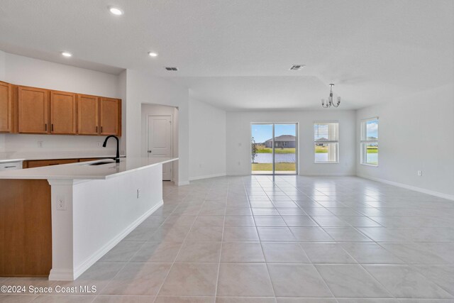 kitchen with a center island with sink, light tile patterned floors, sink, a notable chandelier, and decorative light fixtures