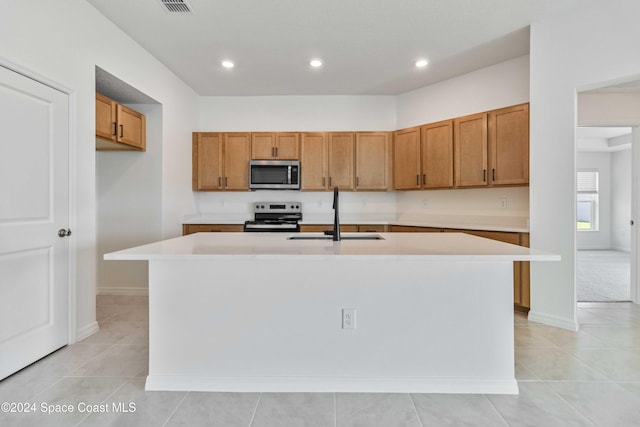 kitchen with light countertops, appliances with stainless steel finishes, a sink, and a kitchen island with sink