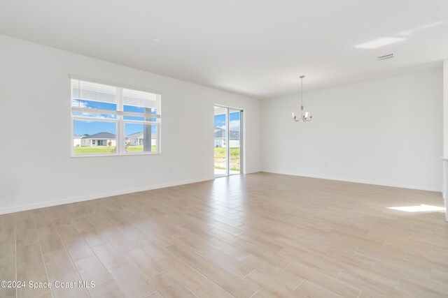 unfurnished room featuring a notable chandelier and light wood-type flooring