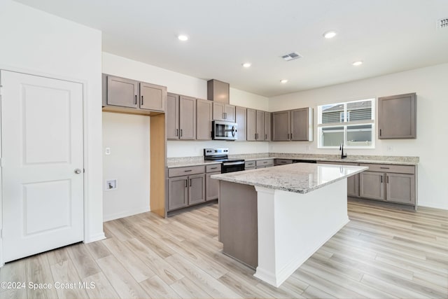 kitchen with light stone countertops, a center island, stainless steel appliances, and light hardwood / wood-style flooring