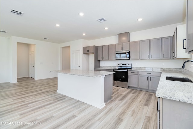 kitchen featuring sink, a center island, light stone counters, appliances with stainless steel finishes, and light wood-type flooring