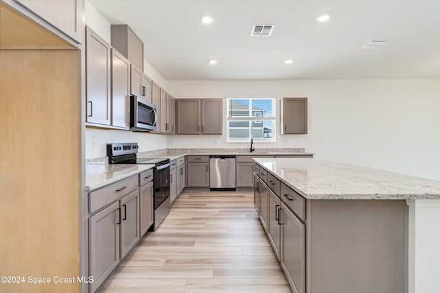 kitchen featuring a center island, sink, appliances with stainless steel finishes, light hardwood / wood-style floors, and light stone counters