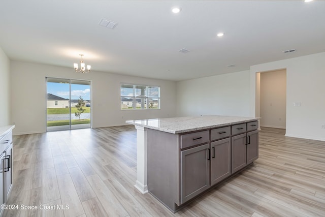 kitchen featuring light stone countertops, a notable chandelier, a center island, light hardwood / wood-style floors, and hanging light fixtures