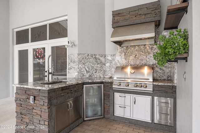 exterior space with decorative backsplash, sink, fridge, light stone countertops, and custom exhaust hood