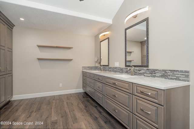 bathroom with decorative backsplash, double vanity, hardwood / wood-style floors, vaulted ceiling, and a textured ceiling