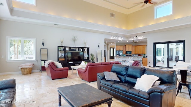 tiled living room featuring a tray ceiling, ceiling fan, ornamental molding, and a towering ceiling