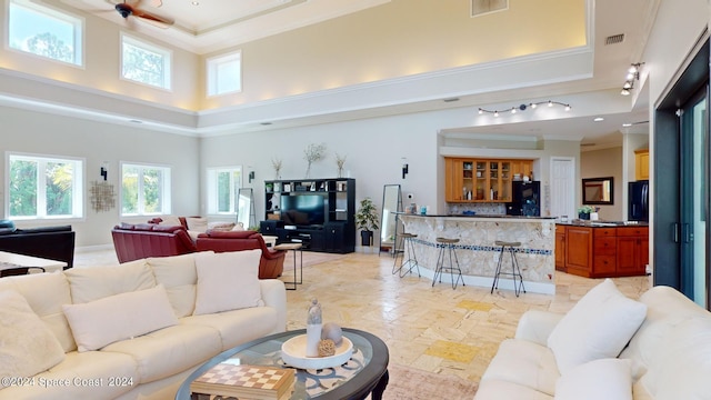 tiled living room with rail lighting, a towering ceiling, ceiling fan, a raised ceiling, and crown molding