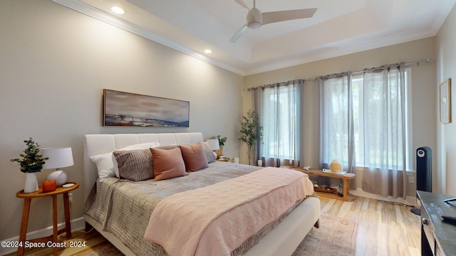 bedroom with light wood-type flooring, a raised ceiling, ornamental molding, and ceiling fan