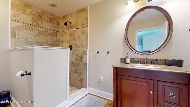 bathroom with hardwood / wood-style flooring, a tile shower, and vanity