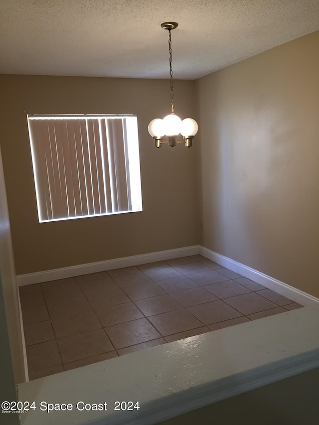 tiled empty room with a textured ceiling and a chandelier