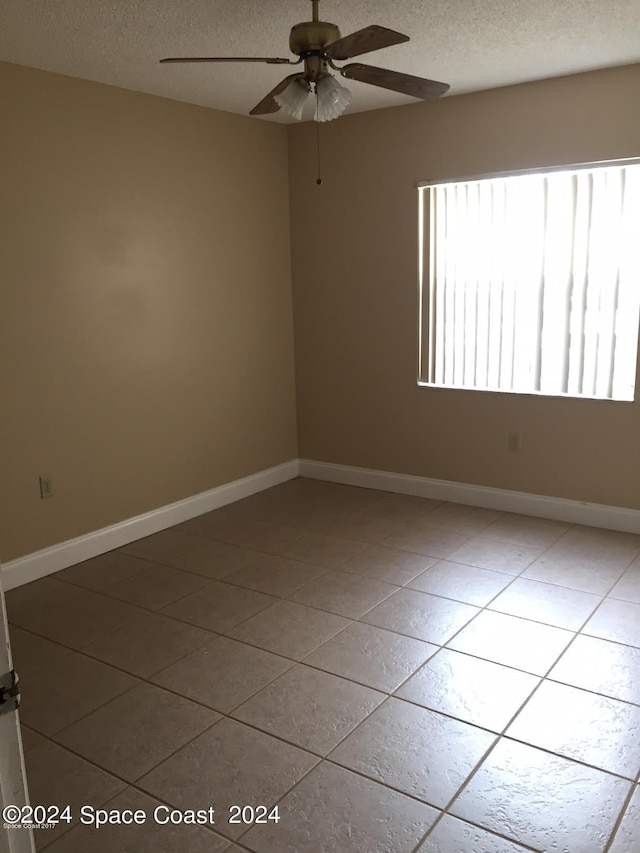 empty room with tile patterned flooring, ceiling fan, and a textured ceiling