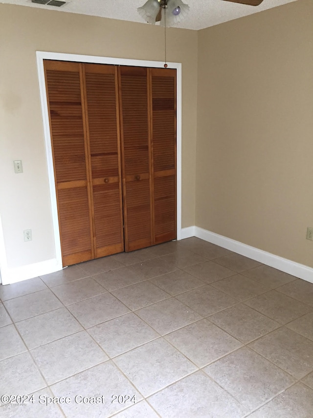 unfurnished bedroom featuring a textured ceiling, a closet, ceiling fan, and light tile patterned floors