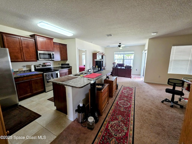 kitchen featuring stainless steel appliances, visible vents, open floor plan, dark countertops, and a center island with sink