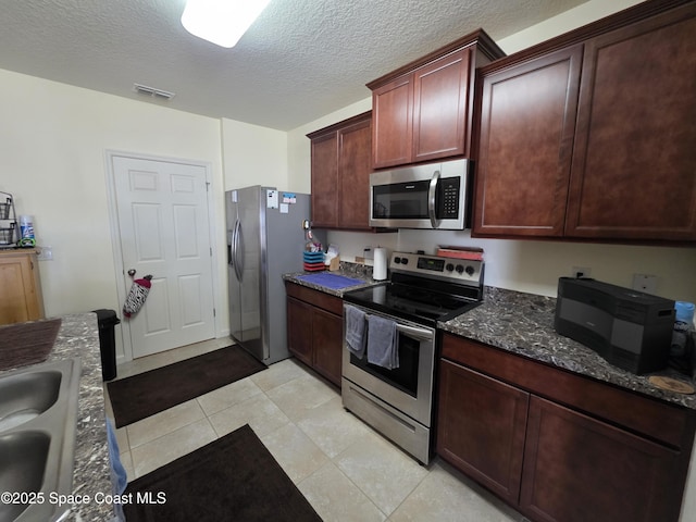 kitchen with stainless steel appliances, visible vents, a sink, a textured ceiling, and dark stone countertops