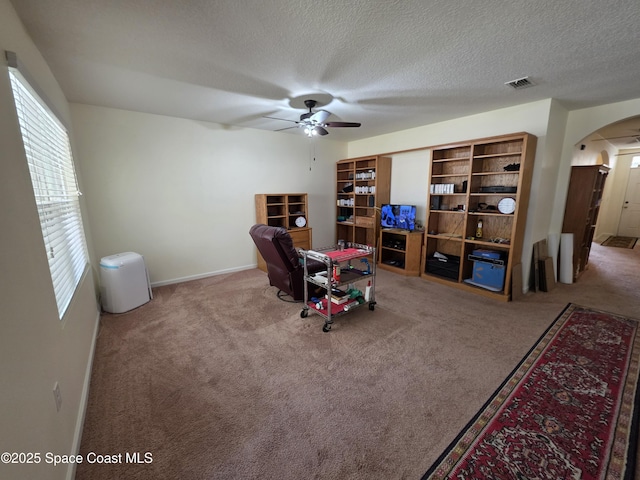 sitting room with visible vents, arched walkways, ceiling fan, a textured ceiling, and carpet floors