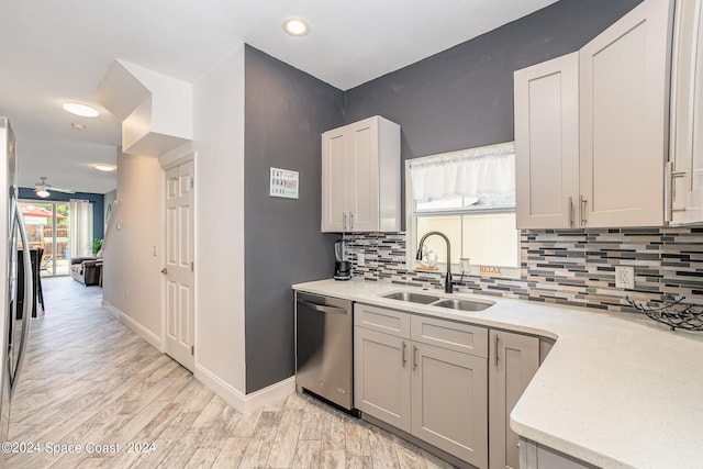 kitchen featuring backsplash, light hardwood / wood-style floors, stainless steel dishwasher, sink, and ceiling fan