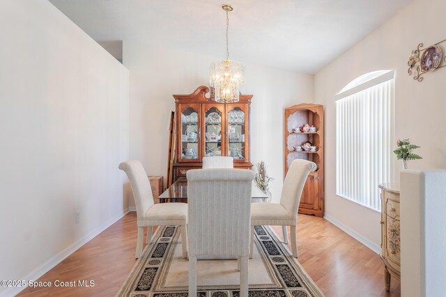 dining space with light wood-type flooring, baseboards, and a notable chandelier