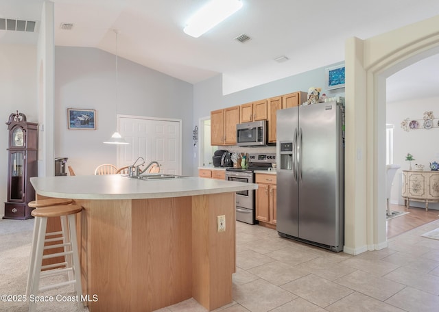 kitchen featuring stainless steel appliances, light countertops, vaulted ceiling, a sink, and a kitchen island with sink