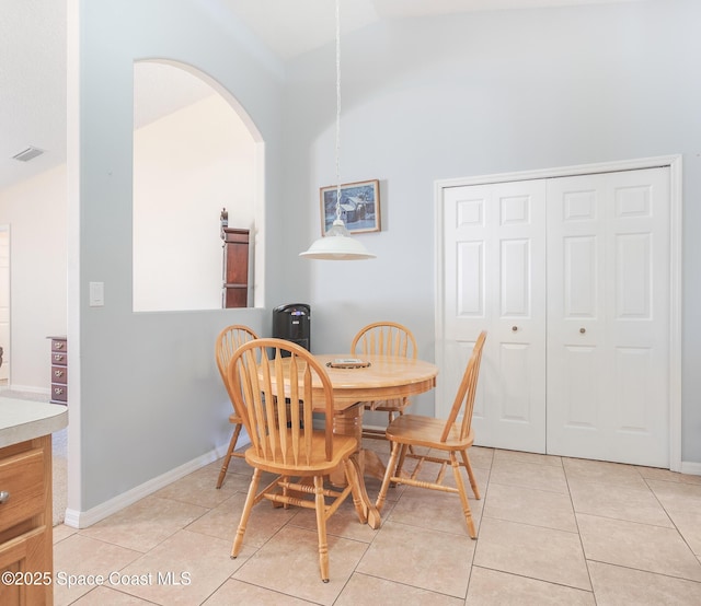 dining space featuring vaulted ceiling, visible vents, light tile patterned floors, arched walkways, and baseboards