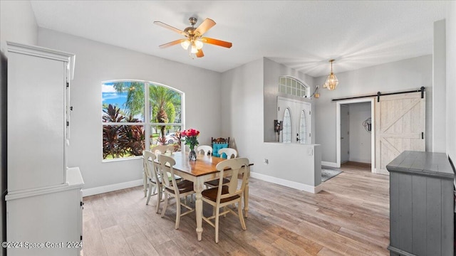 dining space featuring light hardwood / wood-style flooring, ceiling fan, and a barn door