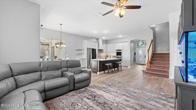 living room featuring ceiling fan with notable chandelier and light wood-type flooring