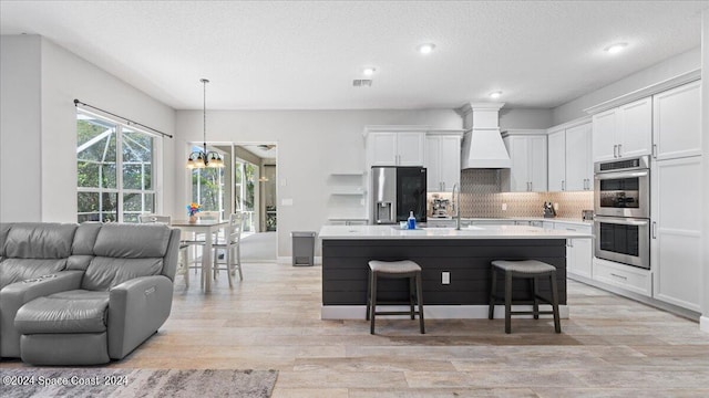 kitchen featuring white cabinets, an island with sink, appliances with stainless steel finishes, and pendant lighting