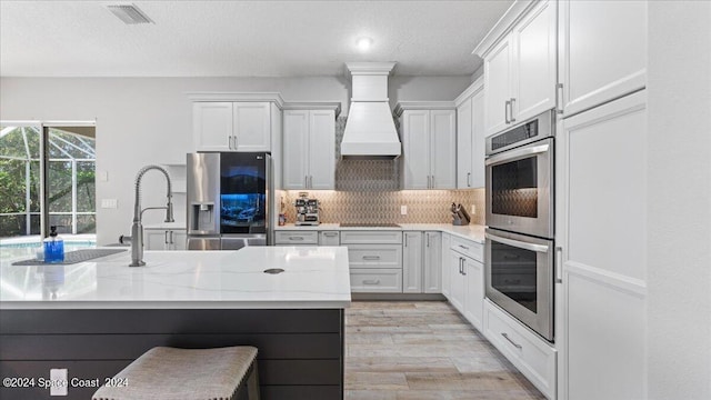 kitchen with light hardwood / wood-style flooring, white cabinetry, appliances with stainless steel finishes, and premium range hood