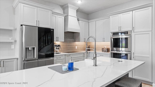 kitchen featuring appliances with stainless steel finishes, light stone counters, tasteful backsplash, a breakfast bar area, and a textured ceiling