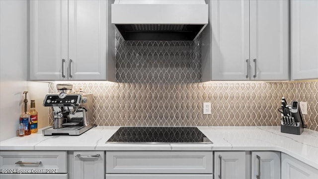 kitchen with light stone counters, black electric cooktop, custom exhaust hood, and backsplash