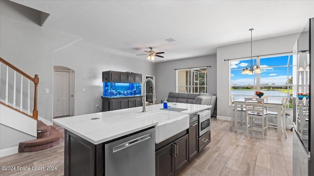 kitchen featuring appliances with stainless steel finishes, a water view, light wood-type flooring, a kitchen island with sink, and sink