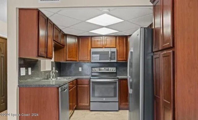 kitchen with light tile patterned floors, appliances with stainless steel finishes, tasteful backsplash, sink, and a paneled ceiling