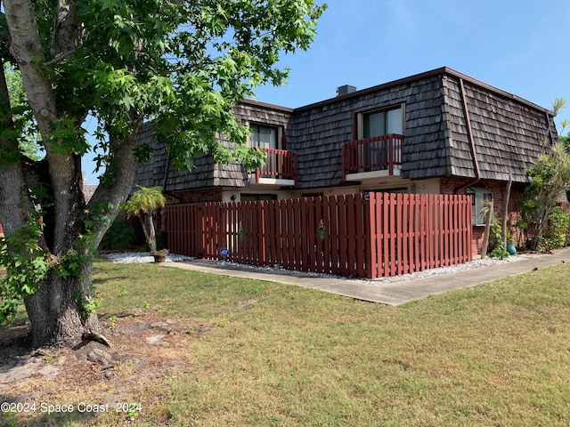 rear view of property featuring a balcony and a yard