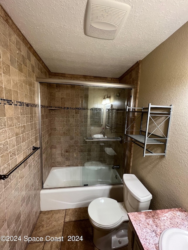 full bathroom with a textured ceiling, vanity, combined bath / shower with glass door, toilet, and tile patterned floors