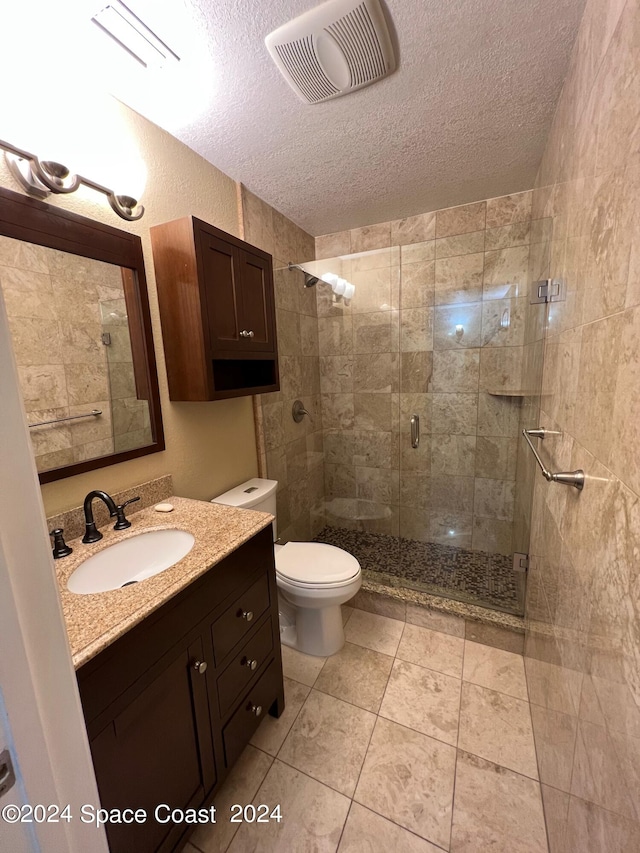 bathroom featuring a shower with door, vanity, a textured ceiling, tile patterned flooring, and toilet