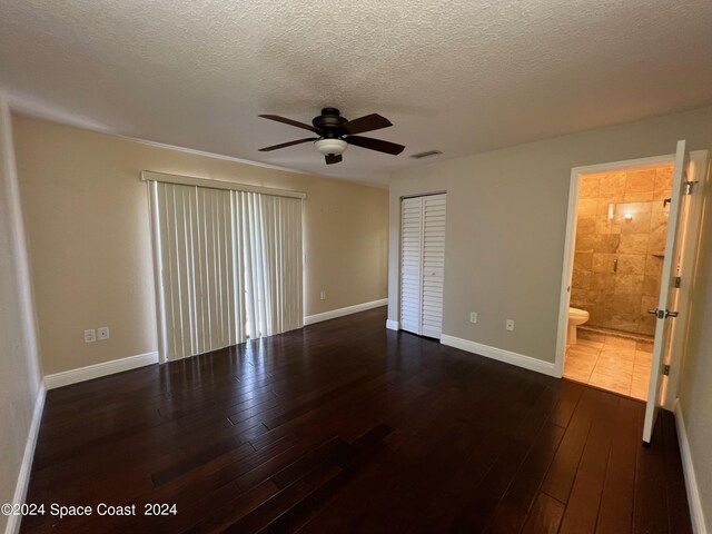 unfurnished bedroom with a textured ceiling, dark hardwood / wood-style flooring, a closet, connected bathroom, and ceiling fan