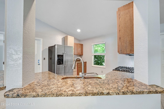 kitchen with stainless steel appliances, lofted ceiling, light stone counters, sink, and light brown cabinets